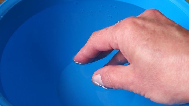 Eine Hand taucht in einen blauen Eimer mit klarem Wasser, bereit zum Fenster putzen mit purem Wasser.