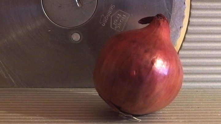 Eine Zwiebel steht vor einer Brotschneidemaschine und wird zum Schneiden vorbereitet, um gleichm&auml;&szlig;ig geschnittene Scheiben zu erhalten.