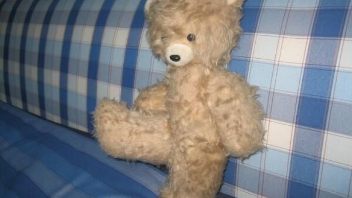 Ein Teddyb&auml;r sitzt auf einer karierten Decke in sanften Blaut&ouml;nen und weckt nostalgische Kindheitserinnerungen.