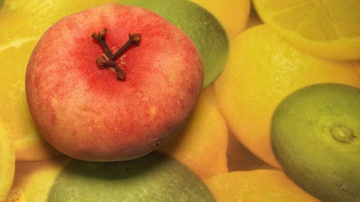 Ein roter Apfel liegt zwischen gelben Zitrusfr&uuml;chten auf einem Tisch, der eine fruchtige Umgebung bildet.