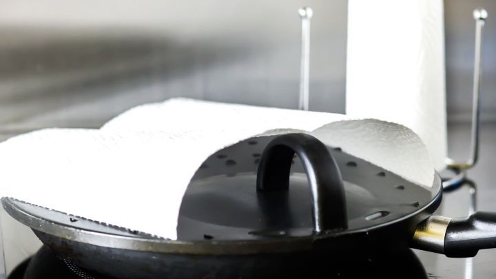 Eine Pfanne mit Spritzschutz liegt auf dem Herd, abgedeckt mit K&uuml;chent&uuml;chern, um Spritzer zu vermeiden.