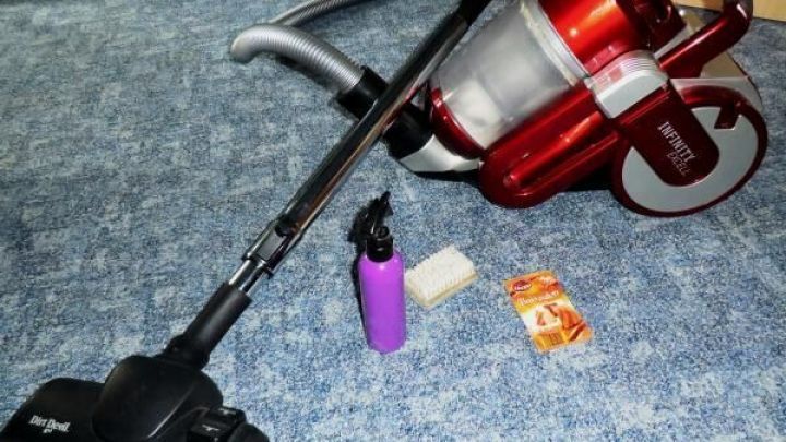 Ein Staubsauger liegt auf einem Teppich, umgeben von einer Reinigungsflasche und Wischt&uuml;chern, bereit zur Teppichreinigung.