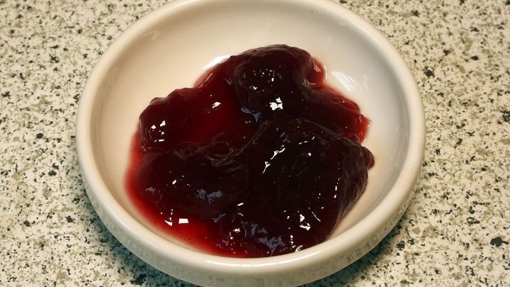 Eine Schale mit roter Sauerkirschmarmelade liegt auf einer grauen Arbeitsplatte und zeigt eine gl&auml;nzende, fruchtige Textur.