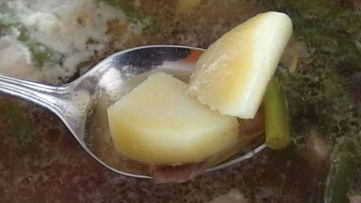 Ein L&ouml;ffel h&auml;lt rohe Kartoffelst&uuml;cke, die in einer salzigen Suppe schwimmen, um den Geschmack auszugleichen.