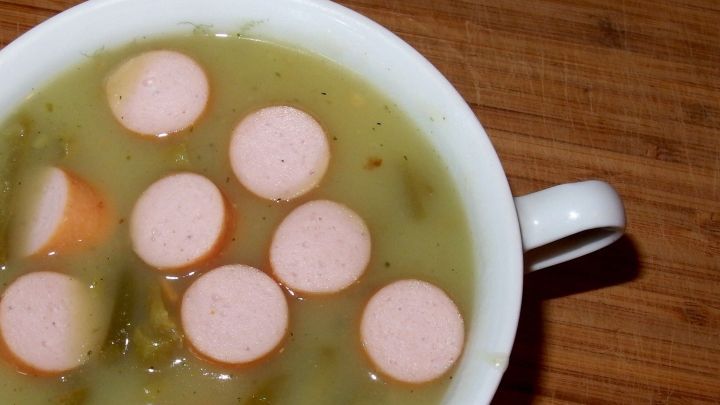 Eine Sch&uuml;ssel Bohnensuppe mit wachsamen W&uuml;rstchen schwimmt in einer hellgr&uuml;nen Br&uuml;he, auf einem Holzuntergrund platziert.