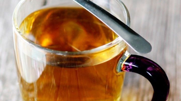 Ein Glas Tee steht auf einem rustikalen Holzuntergrund, w&auml;hrend ein silberner L&ouml;ffel auf dem Rand liegt.