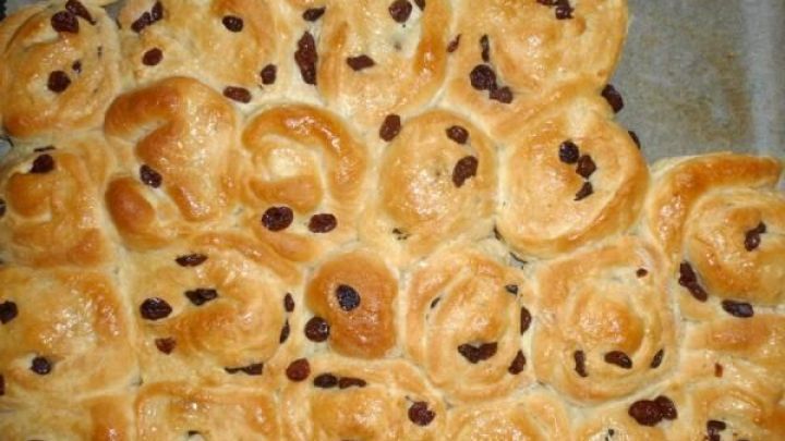 Rosinenschnecken liegen nah beieinander auf einem Backblech. Der Teig ist golden gebacken, verziert mit Rosinen.