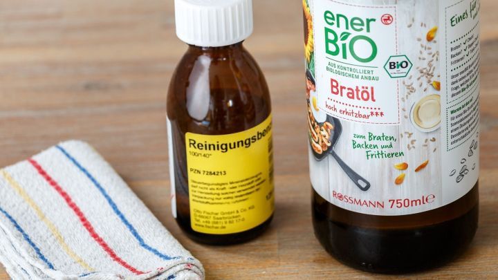 Ein Reinigungsmittel und ein Fl&auml;schchen Leim entfernen vor einem Geschirrtuch auf einer Holzoberfl&auml;che.