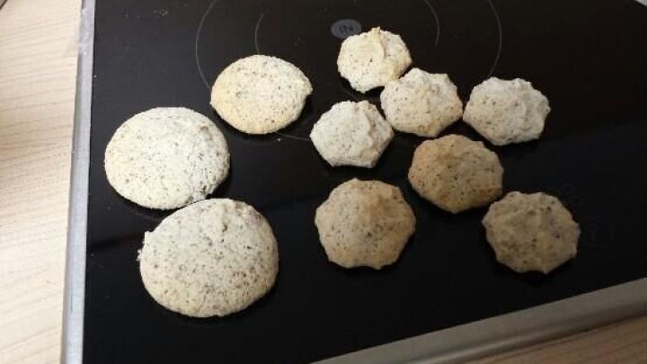 Einige frisch gebackene Makronen liegen auf einer glatten, dunklen Oberfl&auml;che. Sie sind unregelm&auml;&szlig;ig geformt und variieren in der Gr&ouml;&szlig;e.