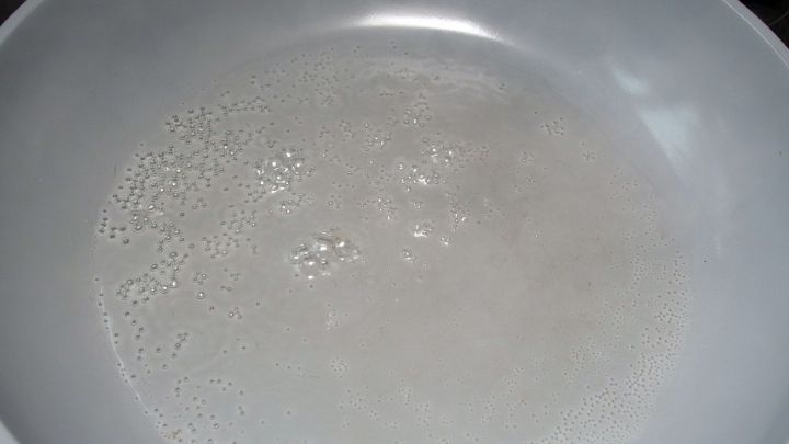 Eine wei&szlig;e Pfanne zeigt kleine Blasen, w&auml;hrend Fleisch ohne Fett br&auml;t. Die W&auml;rmequelle ist kaum sichtbar im Hintergrund.