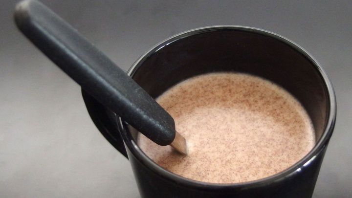 Eine schwarze Tasse mit warmer, schaumiger hei&szlig;er Schokolade und einem L&ouml;ffel in einer dunklen Umgebung.