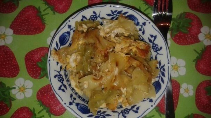 Ein Teller Nudeln mit Gem&uuml;se und einer goldbraunen Kruste liegt auf einem farbenfrohen Erdbeer-Tischdeckenmuster.