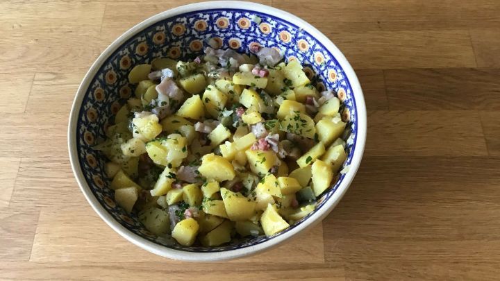 Ein bunter Keramiksch&uuml;ssel enth&auml;lt geschmackvollen Kartoffelsalat mit Fisch, angerichtet auf einer rustikalen Holzoberfl&auml;che.