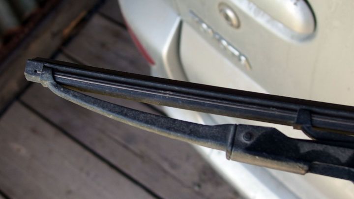 Ein scheibenwischer liegt auf einer dreckigen Autoscheibe, w&auml;hrend er im Hintergrund in einer Au&szlig;enumgebung positioniert ist.