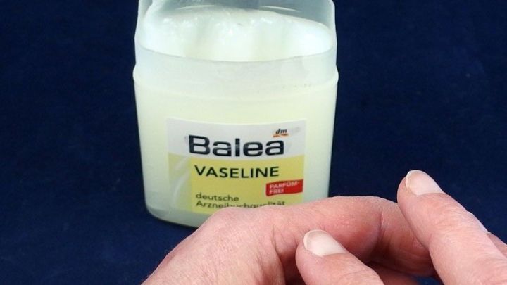Ein Glas Balea Vaseline steht auf einem dunkelblauen Untergrund, w&auml;hrend eine Hand es sanft ber&uuml;hrt, um raue Haut zu behandeln.