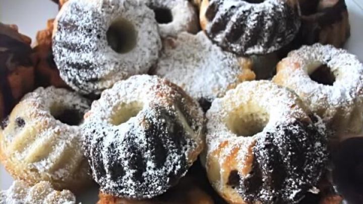 Kleine R&uuml;hrkuchen mit Puderzucker liegen auf einem Teller und wirken einladend in einer hellen K&uuml;chenszene.