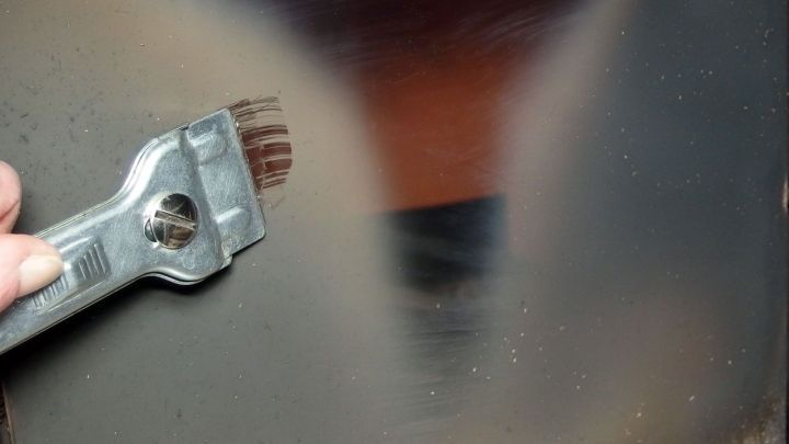 Ein Handwerker reinigt mit einem Werkzeug das Kaminglas, um Schmutz zu entfernen und die Sicht zu verbessern.