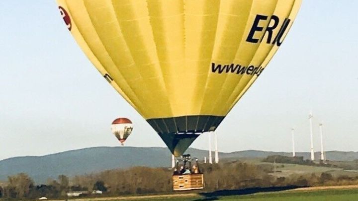 Ein gelber Hei&szlig;luftballon schwebt sanft &uuml;ber eine gr&uuml;ne Wiese, w&auml;hrend der klare Himmel im Hintergrund strahlt.