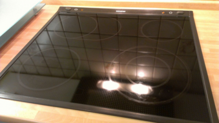 Ein gl&auml;nzendes Glaskeramikfeld liegt auf einem Holzuntergrund, bereit zur Reinigung, mit gutem Licht reflektierend.