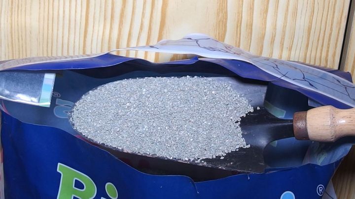 Eine T&uuml;te Katzenstreu steht aufrecht, w&auml;hrend ein L&ouml;ffel das granulierte Material scout und bereit zum Streuen bei Eis und Gl&auml;tte ist.