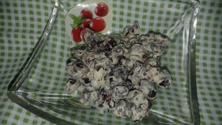 Cranberries mit wei&szlig;er Schokolade liegen in einer Glassch&uuml;ssel und sind auf einem karierten Hintergrund sichtbar.