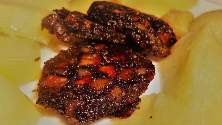 Dunkle, knusprige Himmel und Erde Scheiben liegen auf einem wei&szlig;en Teller, umgeben von gelben Kartoffelst&uuml;cken.