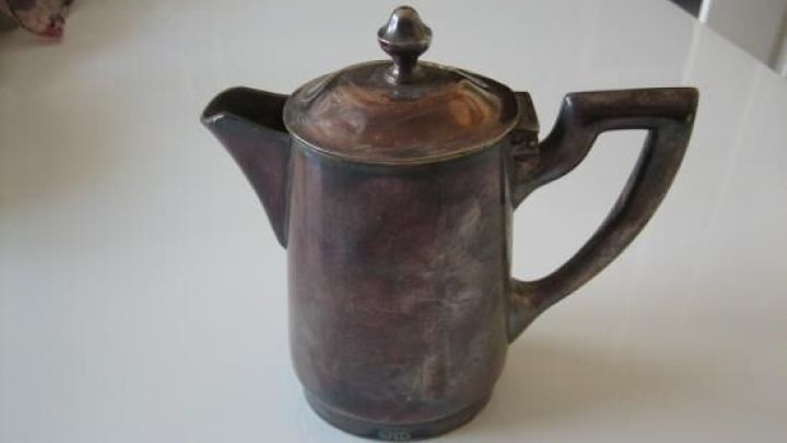 Eine angelaufene Silberkanne steht auf einem wei&szlig;en Tisch, w&auml;hrend sie darauf wartet, poliert zu werden.