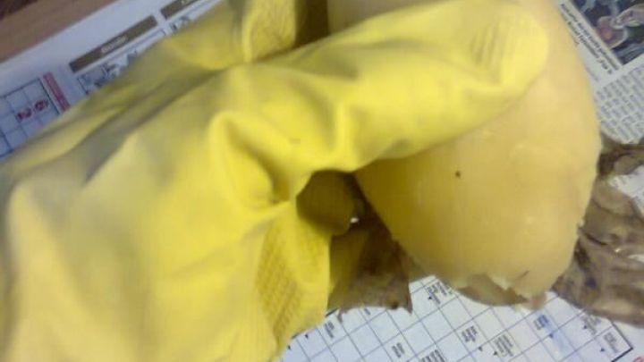 Eine Hand mit gelbem Handschuh sch&auml;lt eine Kartoffel auf einer Zeitungsunterlage, um Fingerverbrennungen zu vermeiden.