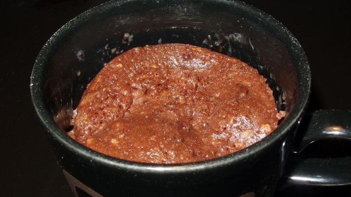 Ein schokoladiger Tassenkuchen steht in einer schwarzen Tasse und sieht luftig und schokoladig aus.