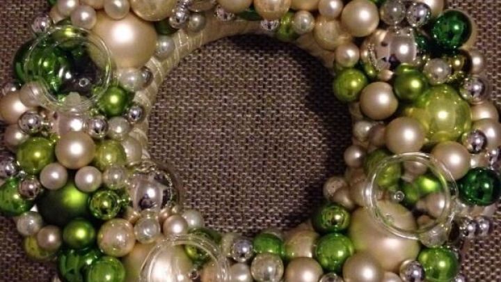 Ein dekorativer Kranz aus Christbaumkugeln in Gr&uuml;nt&ouml;nen und Silber schimmert auf einem gewebten Untergrund.
