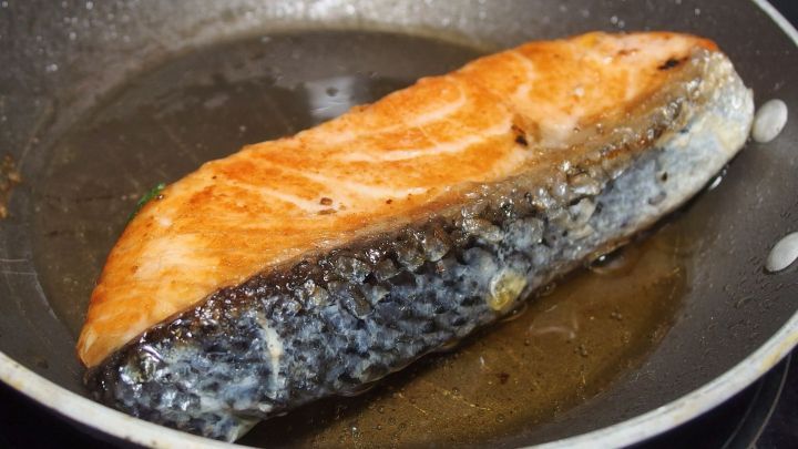 Ein saftiger St&uuml;ck Lachs br&auml;t in einer Pfanne, wodurch starke K&uuml;chenger&uuml;che entstehen. Aromatische D&auml;mpfe steigen auf.