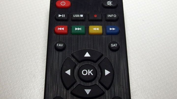 Eine schwarze Fernbedienung liegt auf einer hellen Oberfl&auml;che, w&auml;hrend ihre Tasten f&uuml;r die Steuerung von Ger&auml;ten bereitstehen.