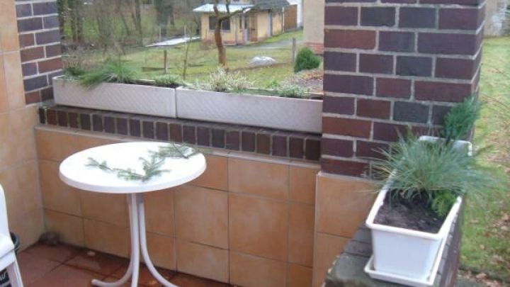 Ein Tisch steht neben einem Balkonkasten, der mit Tannenzweigen zur Stabilisierung gegen den Wind dekoriert ist.