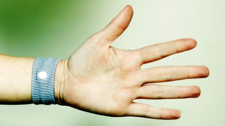 Ein Handgelenk mit einem blauen Sea-Band zur Linderung von Schwangerschafts&uuml;belkeit ist vor einem unscharfen, gr&uuml;nen Hintergrund zu sehen.