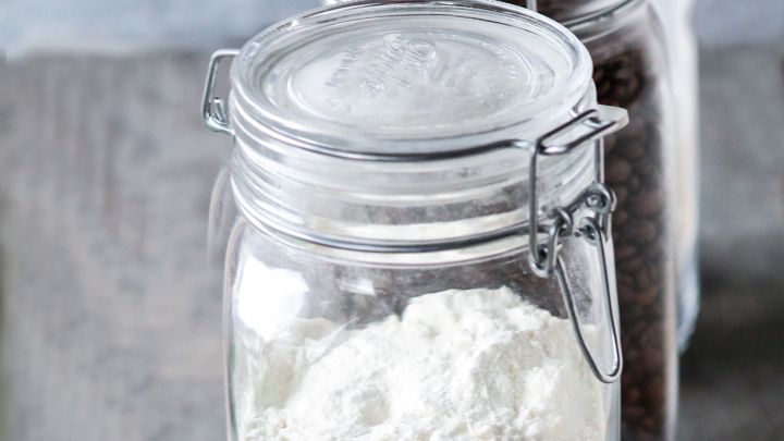 Ein transparentes Einmachglas ist mit Mehl gef&uuml;llt, beschriftet und steht neben anderen gef&uuml;llten Gl&auml;sern auf einem Tisch.