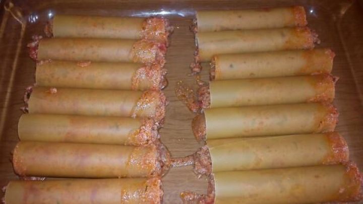 Cannelloni liegen in einer Glasauflaufform, gef&uuml;llt mit Hack-Tomaten-Mischung, bereit zum Kochen im Ofen.