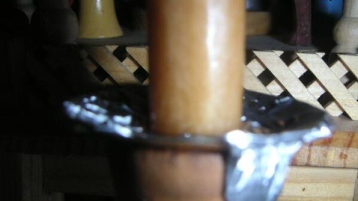 Ein Kerzenhalter aus Holz h&auml;lt eine brennende Kerze, umgeben von Wachsresten, die in einem metallenen Einsatz gesammelt sind.