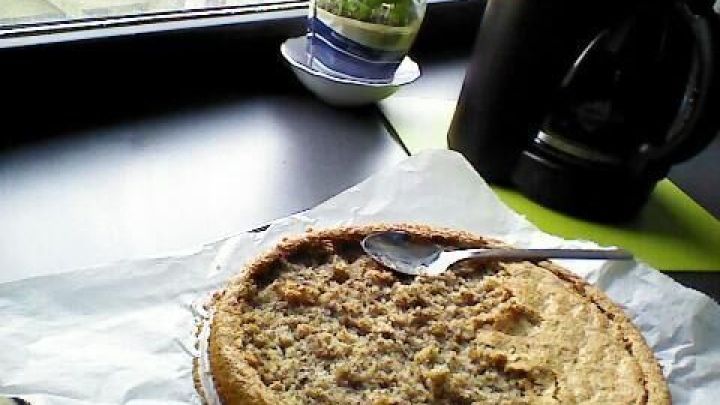 Eine Cappuccino-Torte mit einem L&ouml;ffel auf Backpapier, neben einer Kaffeemaschine auf der Fensterbank. Im Hintergrund steht ein Basilikumtopf.