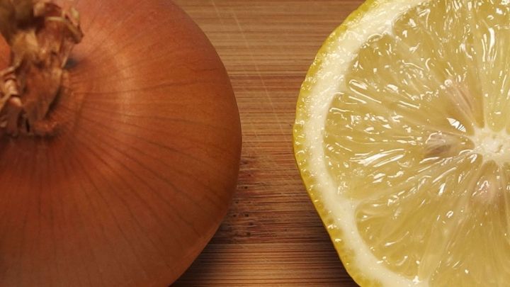 Eine Zwiebel liegt neben einer halbierten Zitrone auf einem Holzbrett, beide bereit f&uuml;r die Zubereitung.