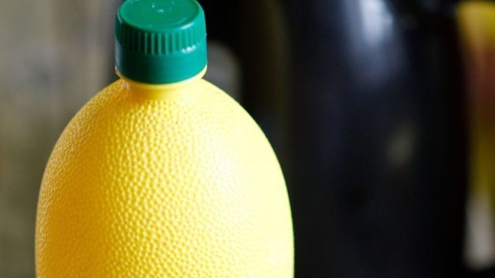 Eine gelbe Flasche mit gr&uuml;nem Deckel steht im Vordergrund, w&auml;hrend ein schwarzer Wasserkocher im Hintergrund sichtbar ist.