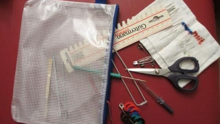 Eine durchsichtige Rei&szlig;verschlusstasche liegt auf einem roten Untergrund und enth&auml;lt verschiedene Handarbeitsutensilien.