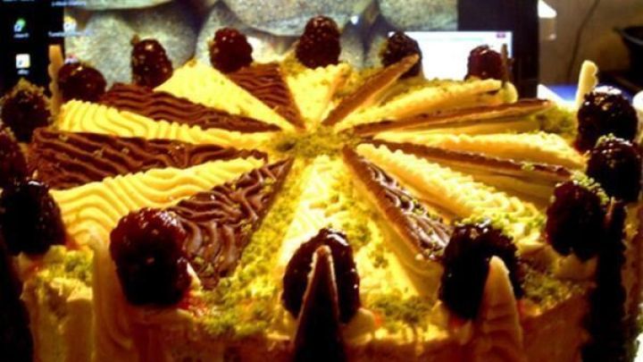 Eine dekorative Waldbeere-Ganache-Torte mit verschiedenen Schichten wird auf einem Tisch pr&auml;sentiert, umgeben von einer dunklen Kulisse.