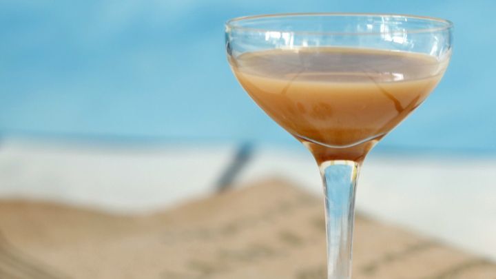 Ein elegantes Glas mit Nusslik&ouml;r steht auf einem Tisch, umgeben von ganzen N&uuml;ssen und einem neutralen Hintergrund.