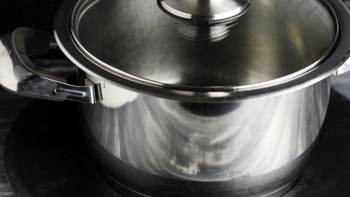 Ein gl&auml;nzender Edelstahltopf steht auf einem schwarzen Untersetzer und wartet darauf, gereinigt zu werden.