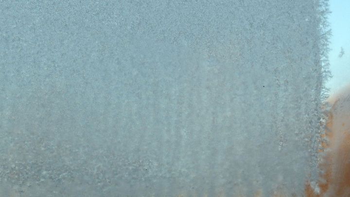 Eine vereiste Windschutzscheibe zeigt eisige Kristalle, die die Sicht beeintr&auml;chtigen, umgeben von unscharfen Hintergr&uuml;nden.