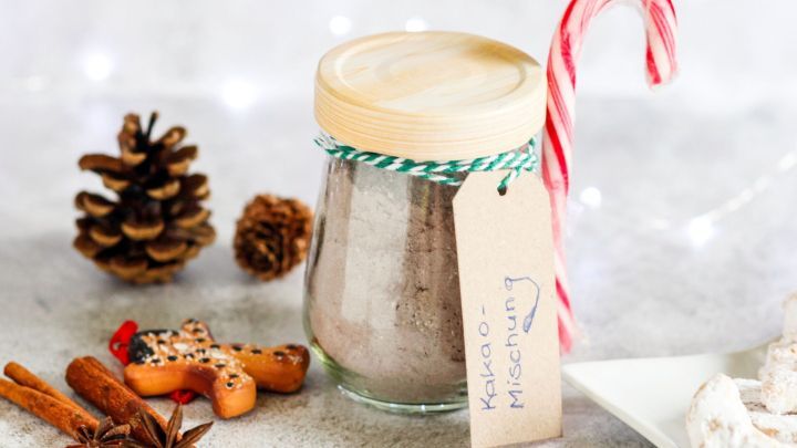 Ein Glas Weihnachtskakao steht auf einem festlichen Tisch, verziert mit einem Zuckerstangen-Strohhalm und Gew&uuml;rzen.