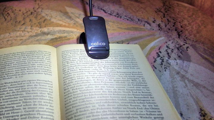 Eine Leselampe beleuchtet eine ge&ouml;ffnete Buchseite, w&auml;hrend eine beruhigende Atmosph&auml;re zum leichteren Einschlafen beitr&auml;gt.