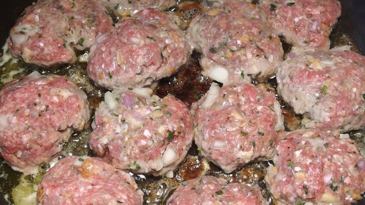 Bouletten braten in einer Pfanne, umgeben von frischem Gem&uuml;se, bieten eine herzhafte Mahlzeit in geschmackvollem Umfeld.