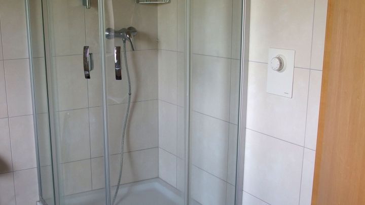 Eine durchsichtige Duschkabine steht in einem Badezimmer, mit Fliesenw&auml;nden und einem Duschkopf, bereit zur Nutzung.