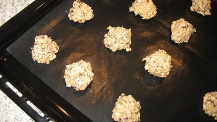 Schokoladen-Haferflocken-Cookies mit Sonnenblumenkernen sind in kleinen Portionen auf einem Blech angeordnet und bereit zum Backen.
